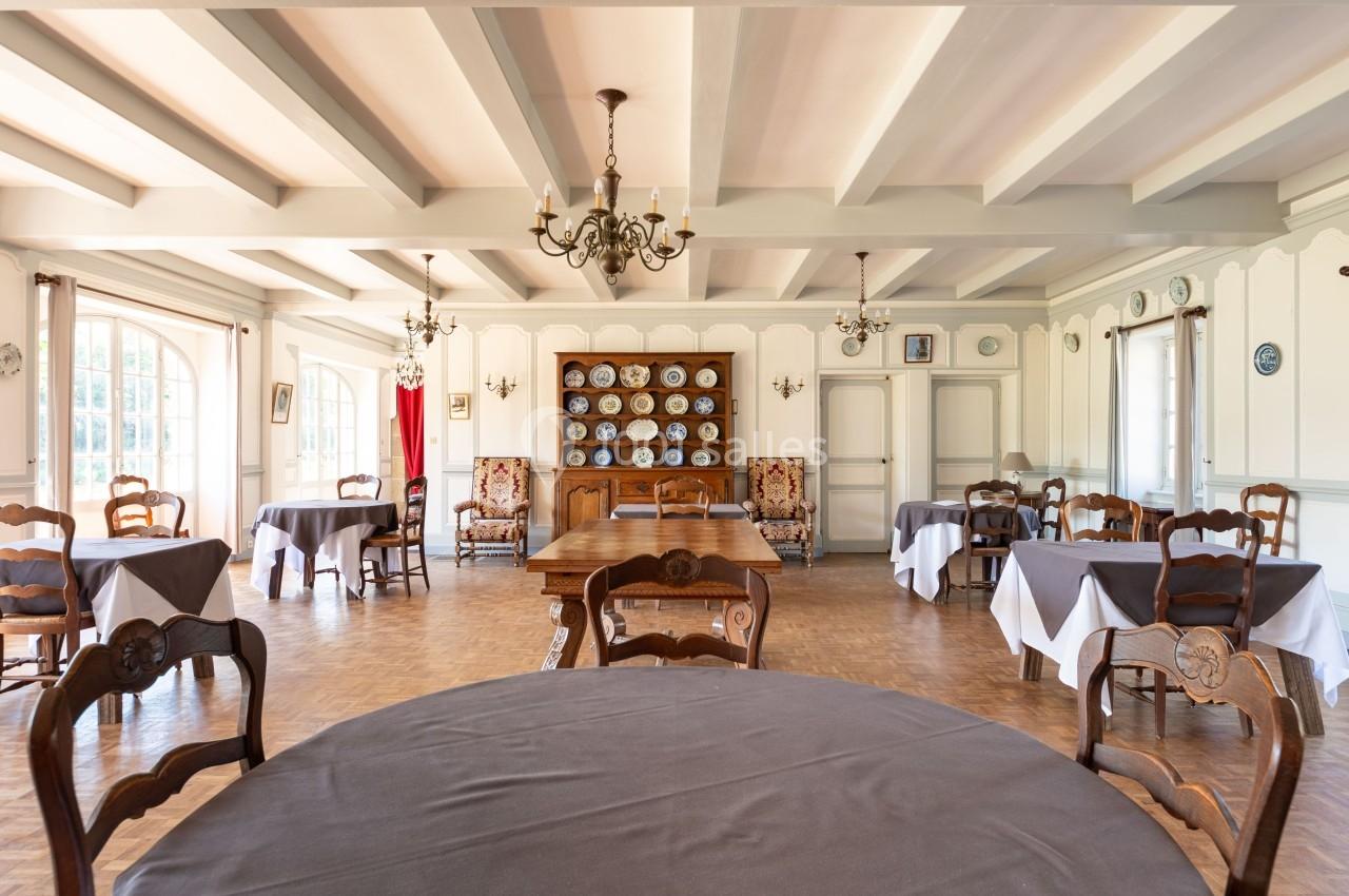 Salle à manger lumineuse avec tables recouvertes de nappes grises, chaises en bois et vaisselier en arrière-plan.