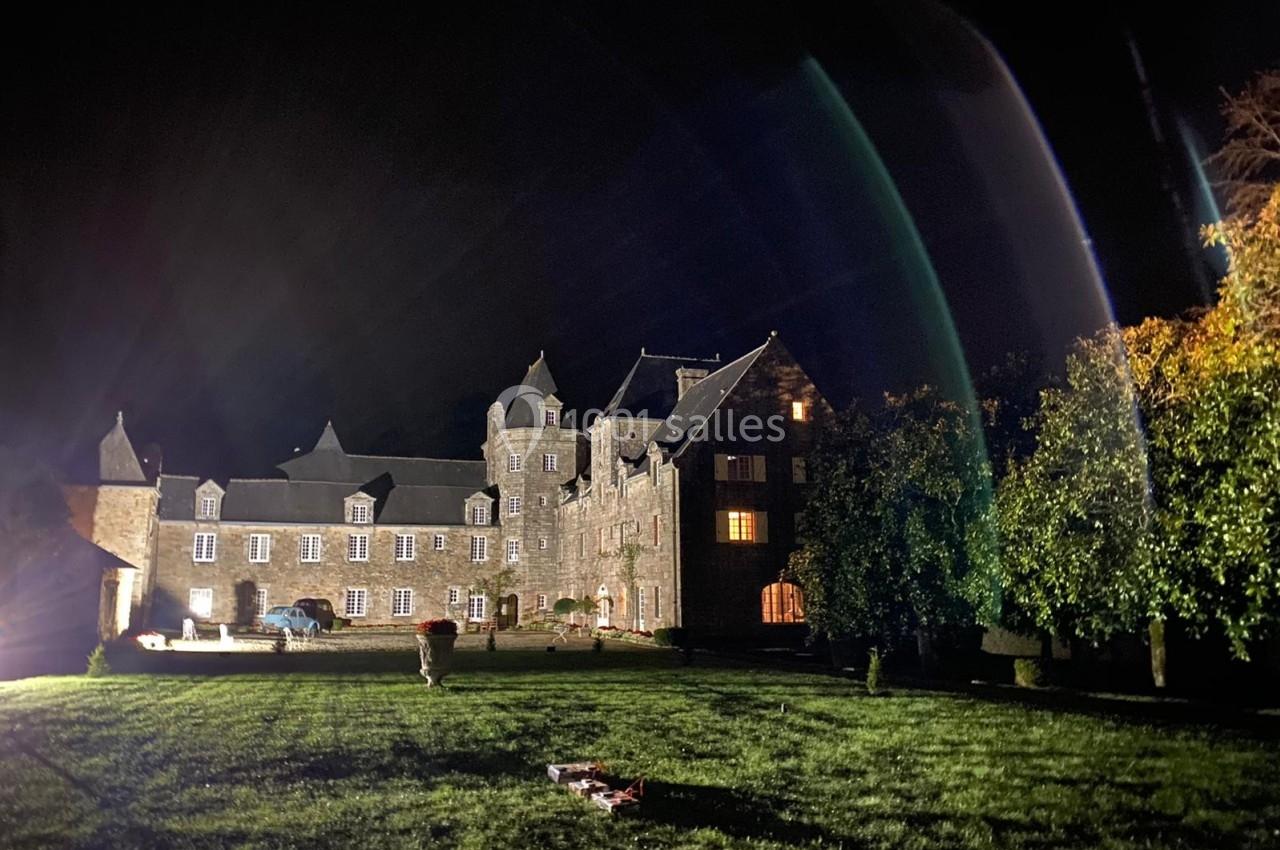 Façade éclairée d'un grand bâtiment en pierre de style ancien, entouré d'une pelouse, de nuit.
