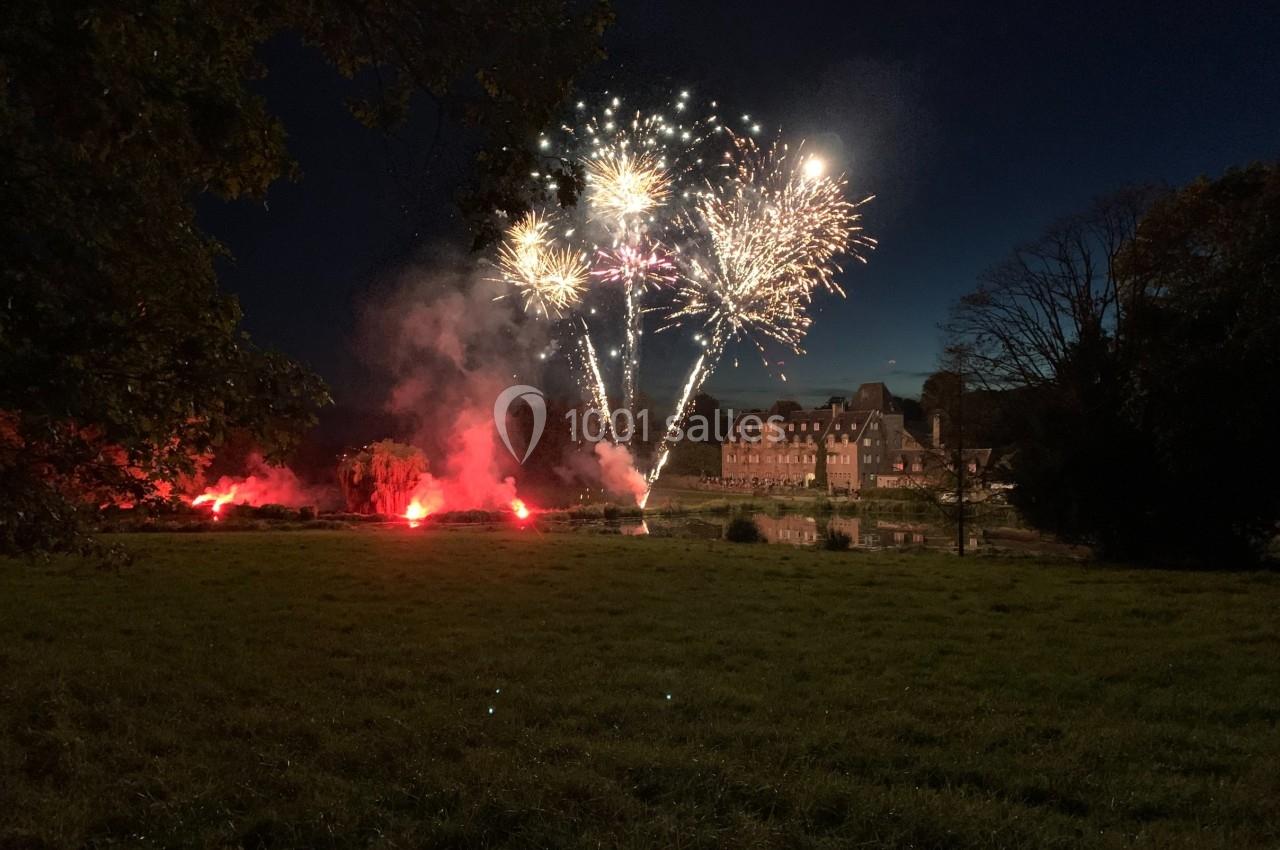 Feu d'artifice illuminant le ciel nocturne au-dessus d'un bâtiment en briques, entouré d'arbres et d'une pelouse.
