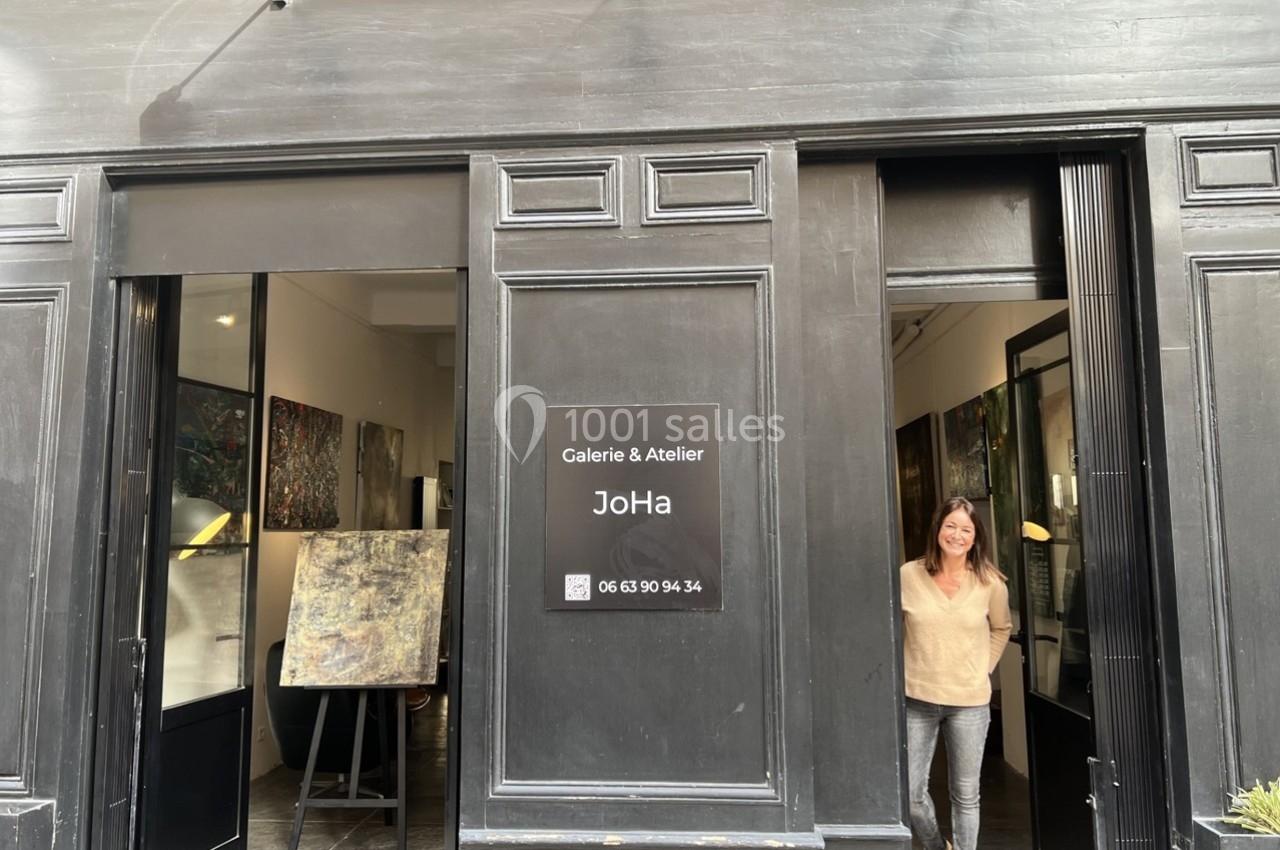 Façade d'une galerie d'art avec une femme souriante debout dans l'encadrement de la porte.