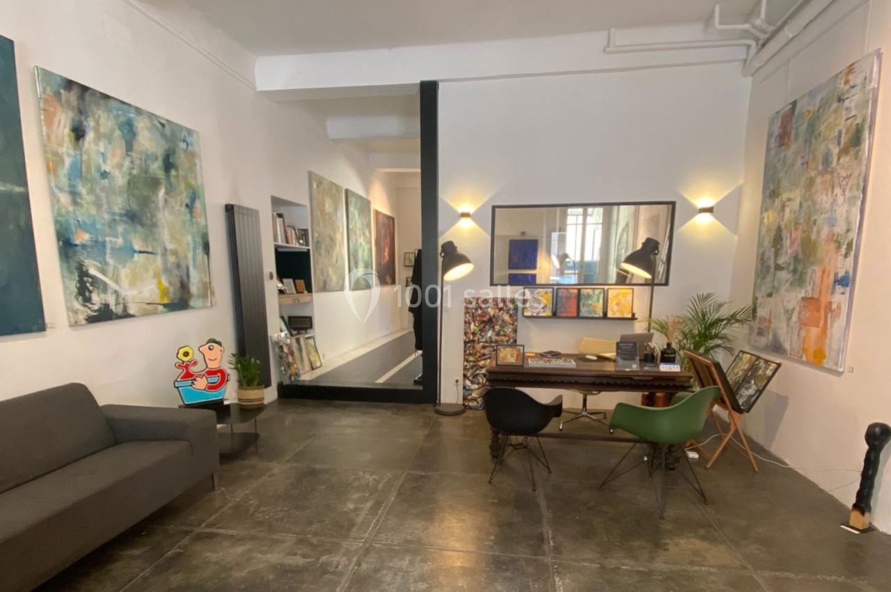Espace intérieur lumineux avec des œuvres d'art accrochées aux murs, un canapé et un bureau avec des chaises design.