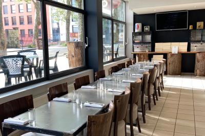 Miniature Location salle Lyon 9 (Rhône) - Le Petit Marché d'Une Faim d'Apprendre #16 Salle lumineuse avec grandes baies vitrées, tables en bois et vue sur une rue calme bordée de bâtiments.