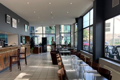 Miniature Location salle Lyon 9 (Rhône) - Le Petit Marché d'Une Faim d'Apprendre #11 Salle lumineuse avec grandes baies vitrées, tables en bois et vue sur une rue calme bordée de bâtiments.