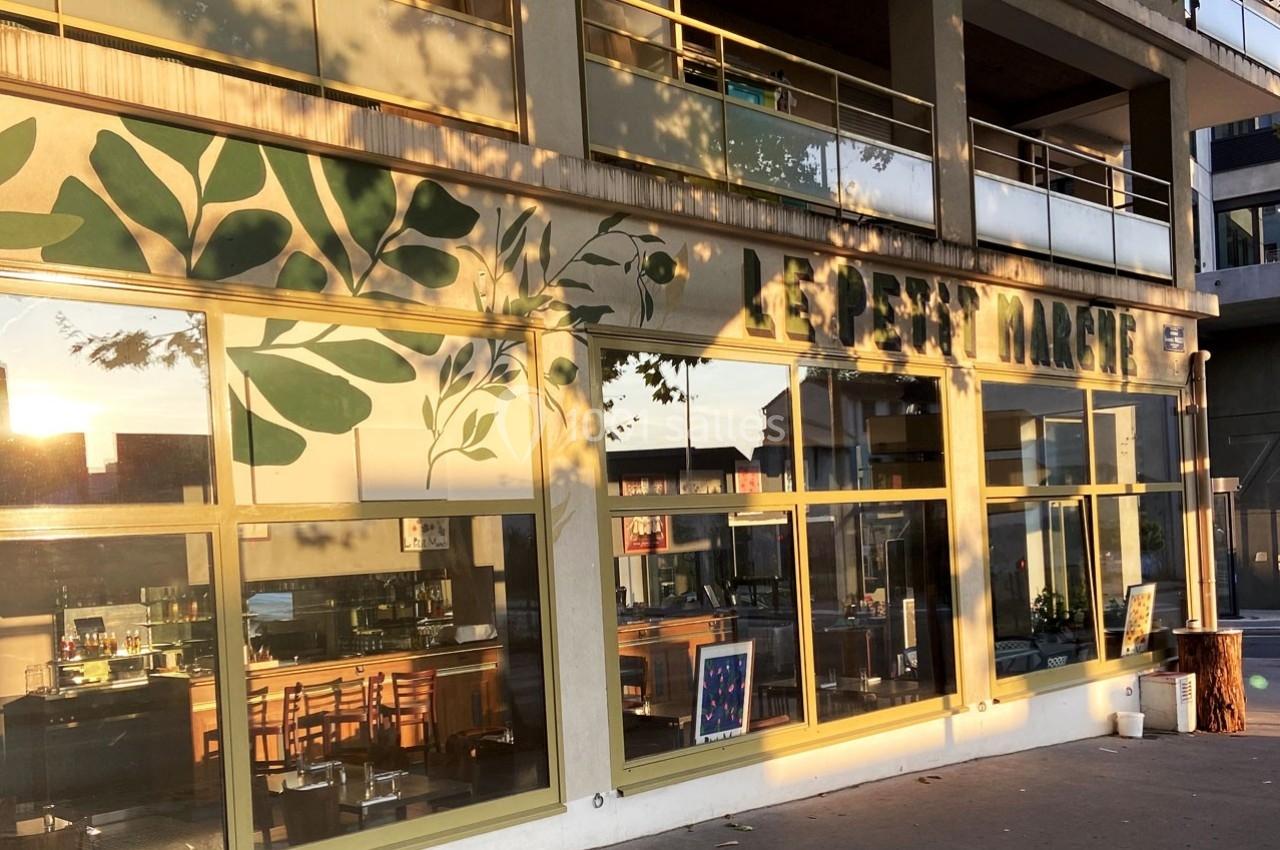 Façade d'un café avec de grandes baies vitrées, décorée de motifs végétaux, éclairée par une lumière de fin de journée.