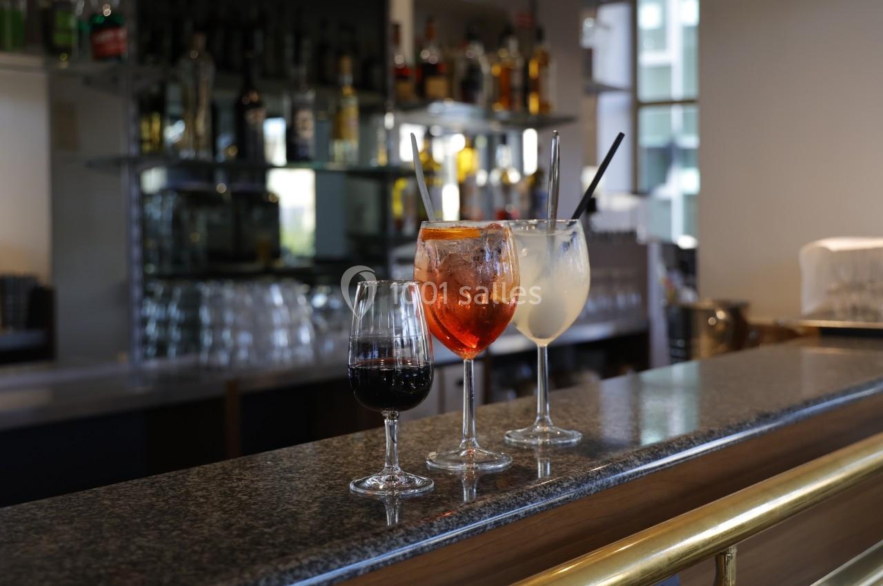 Trois verres de boissons variées posés sur un comptoir de bar, avec des bouteilles en arrière-plan.