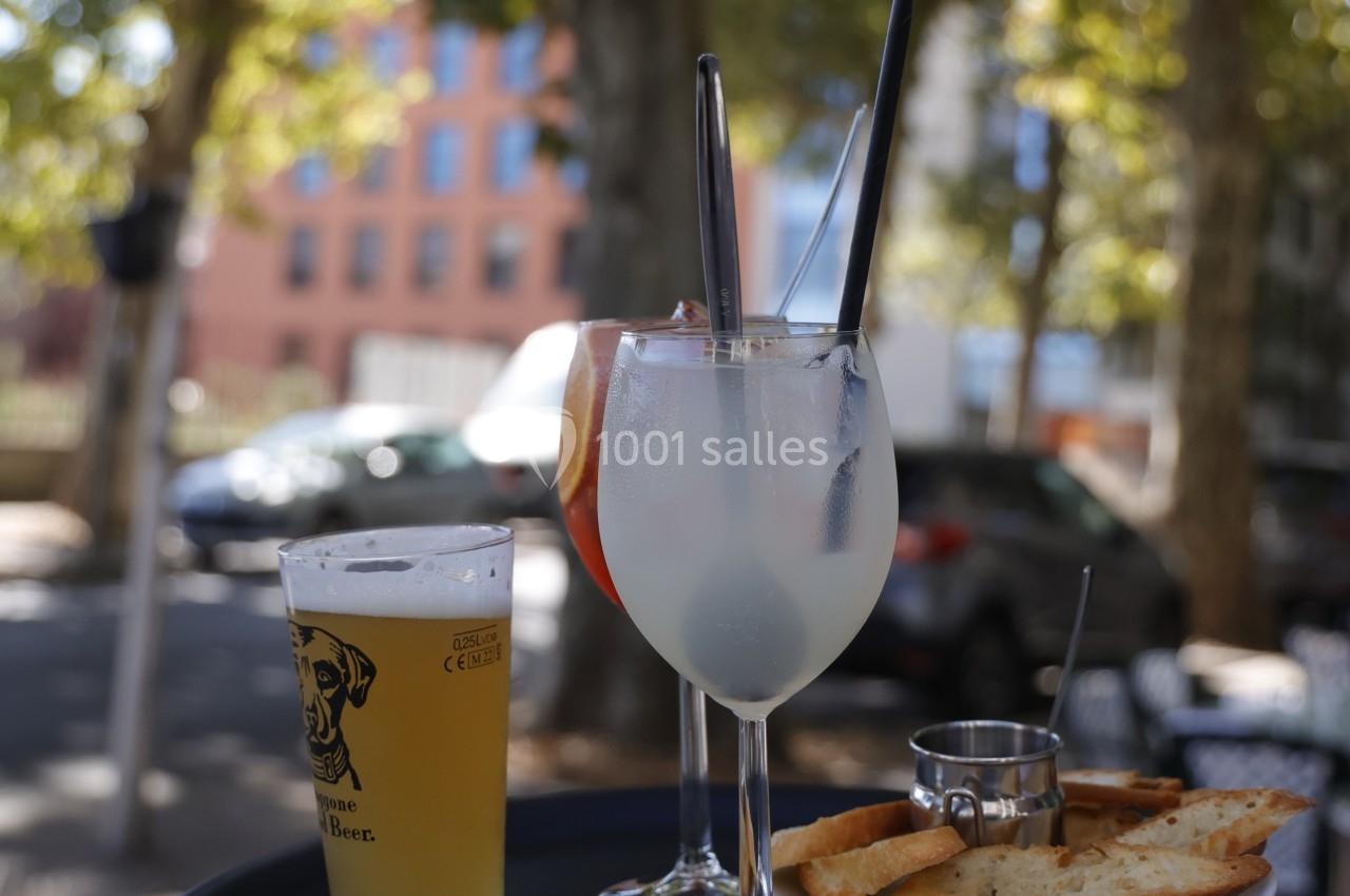 Verres de boissons fraîches sur une table en terrasse, avec des arbres et des bâtiments en arrière-plan.