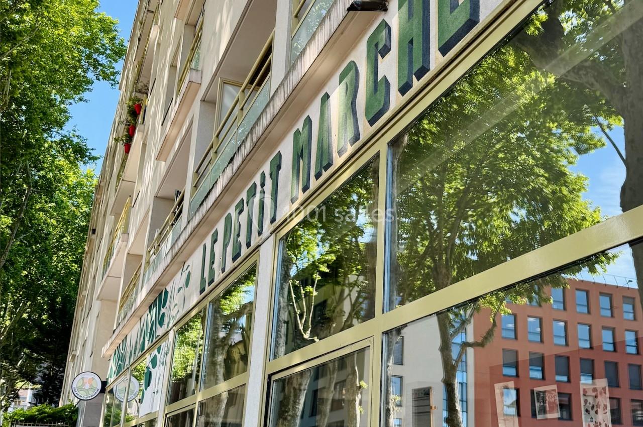 Façade d'un immeuble avec une devanture vitrée et l'inscription ’Marché’ reflétant des arbres et des bâtiments voisins.
