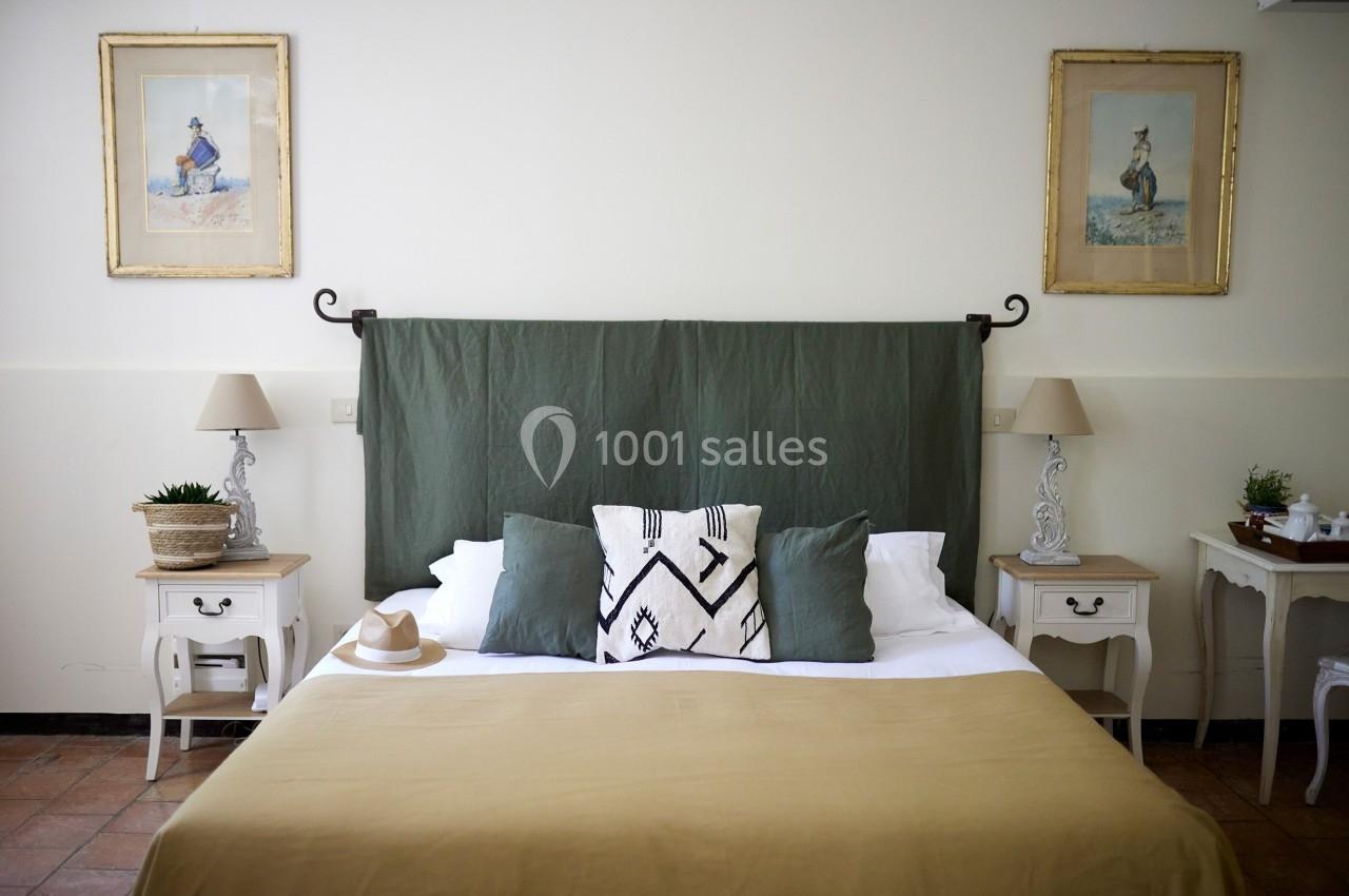 Lit double avec drap beige, coussins décoratifs, et tête de lit verte, encadré par deux tables de chevet et lampes.