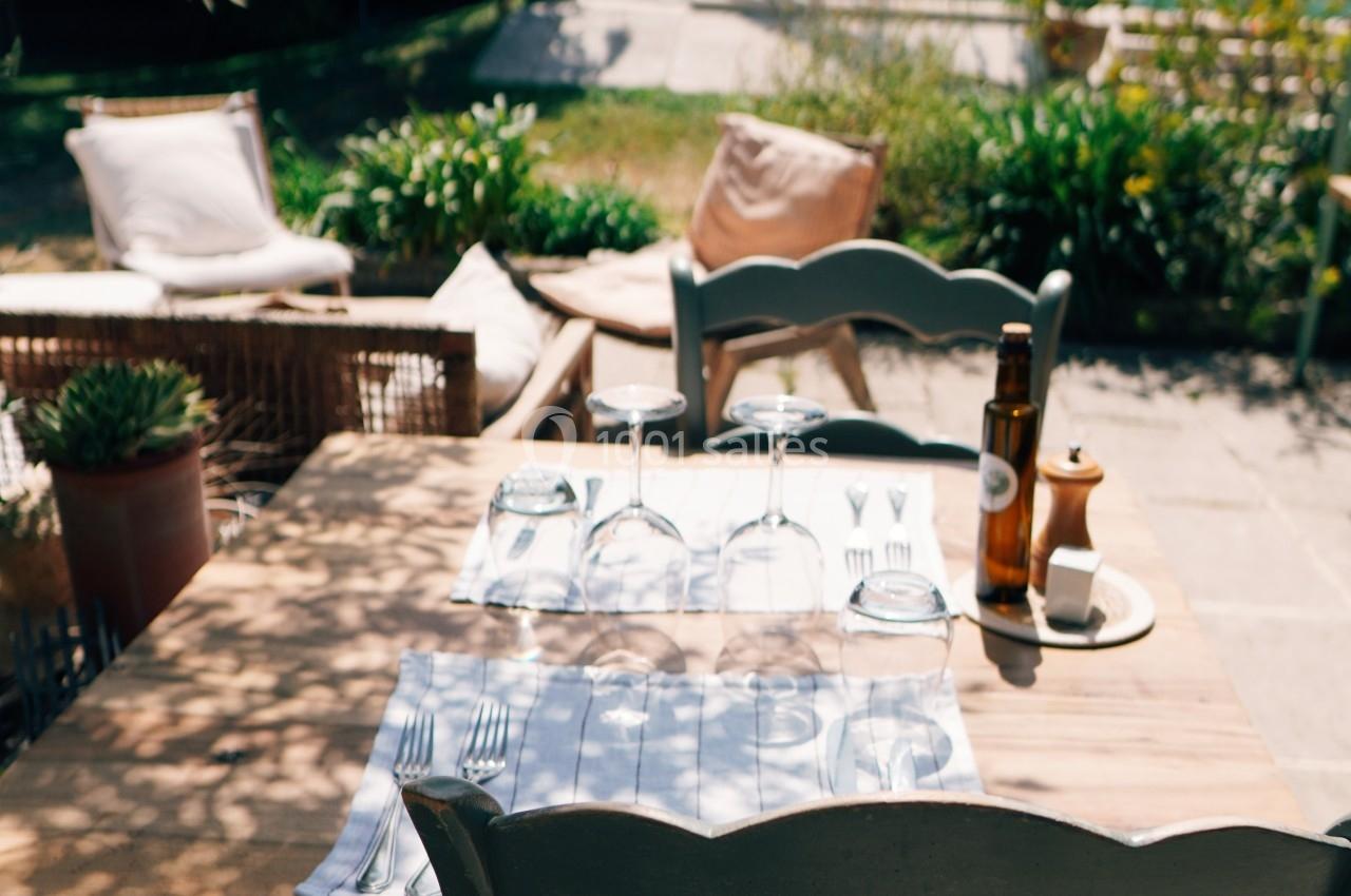 Table en bois dressée avec des couverts et des verres, située en extérieur près d'un jardin et d'une piscine.