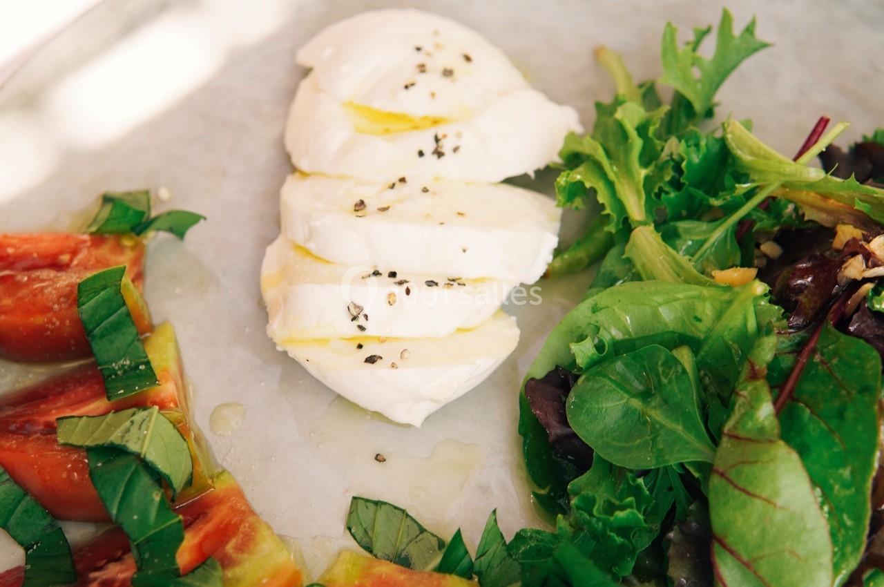 Assiette avec tranches de tomates, mozzarella assaisonnée et salade verte sur une table lumineuse.