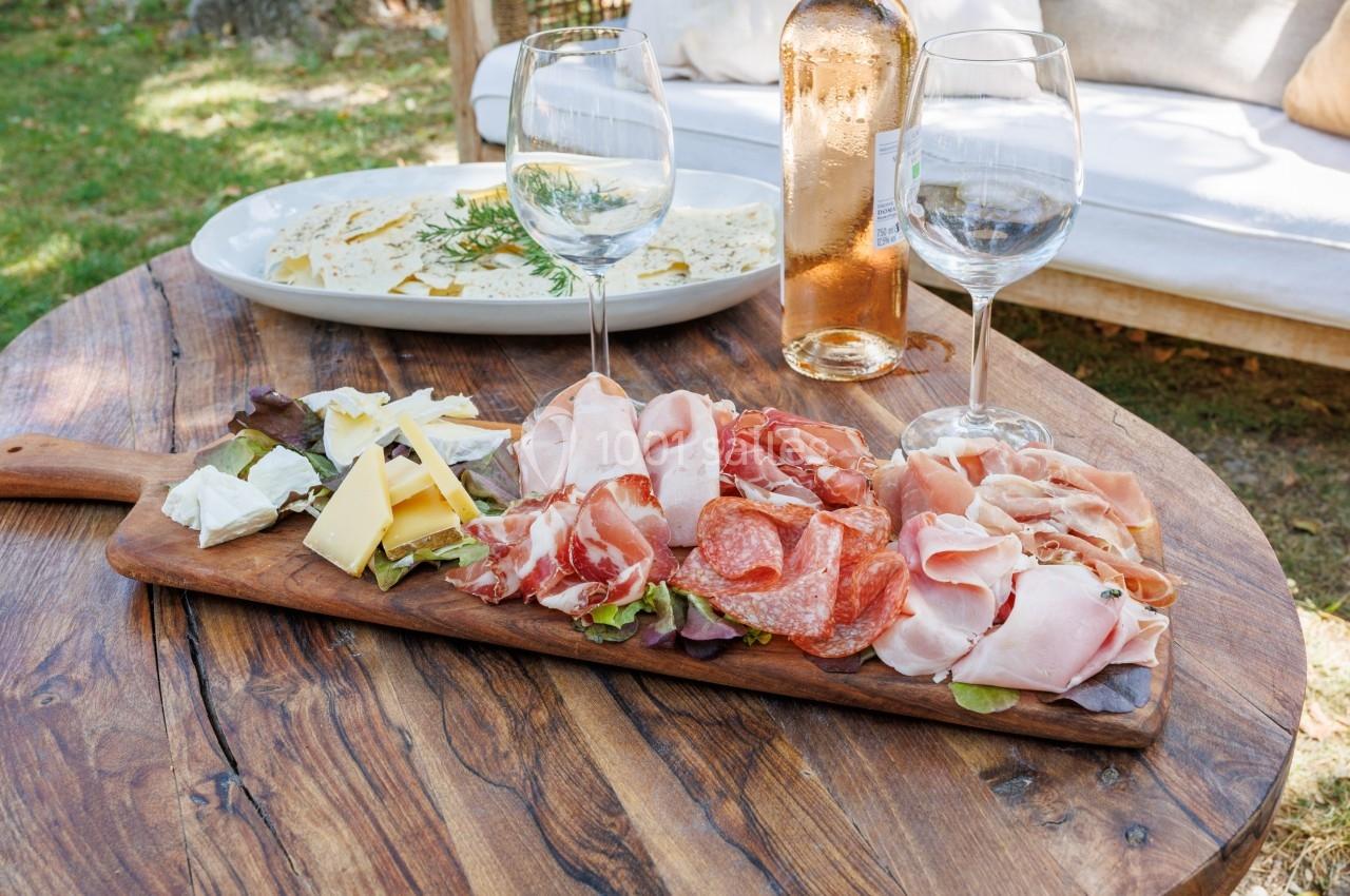 Plateau de charcuterie et fromages variés sur une planche en bois, accompagné de vin rosé et pain, en extérieur.