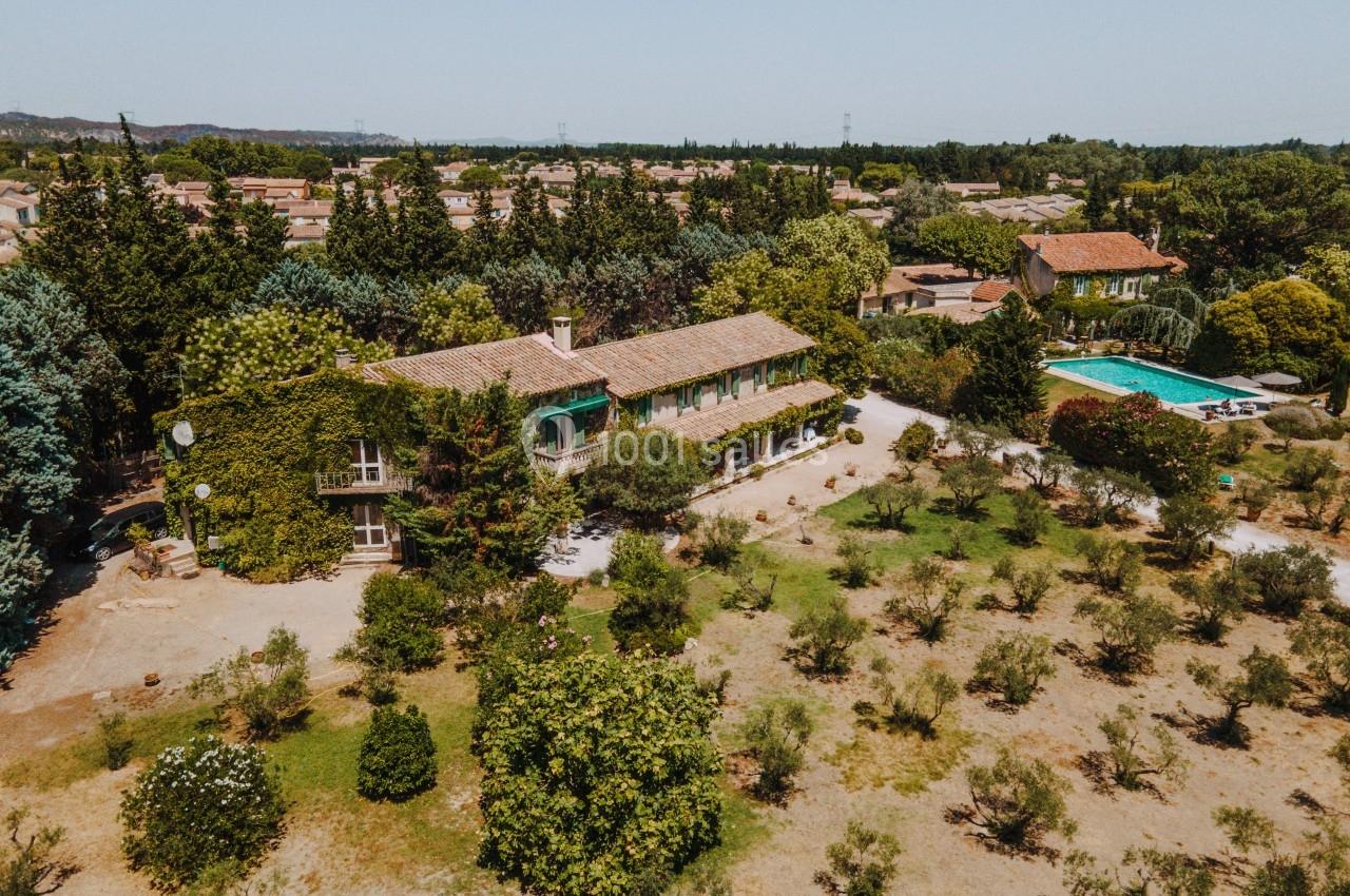 Vue aérienne d'une maison entourée d'arbres, avec une piscine et un jardin dans un environnement rural.