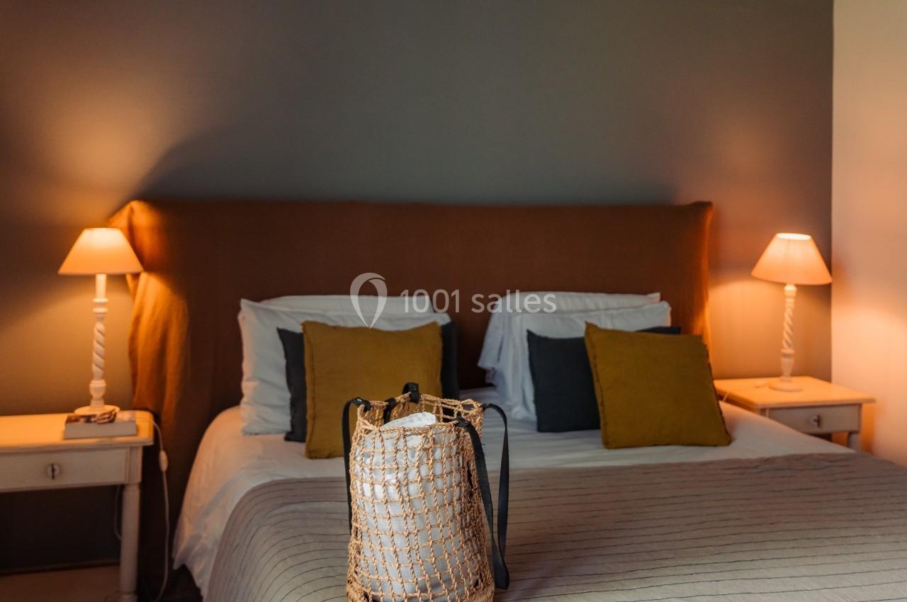Lit double avec tête de lit orange, tables de chevet, lampes allumées et un sac en osier posé sur le couvre-lit.