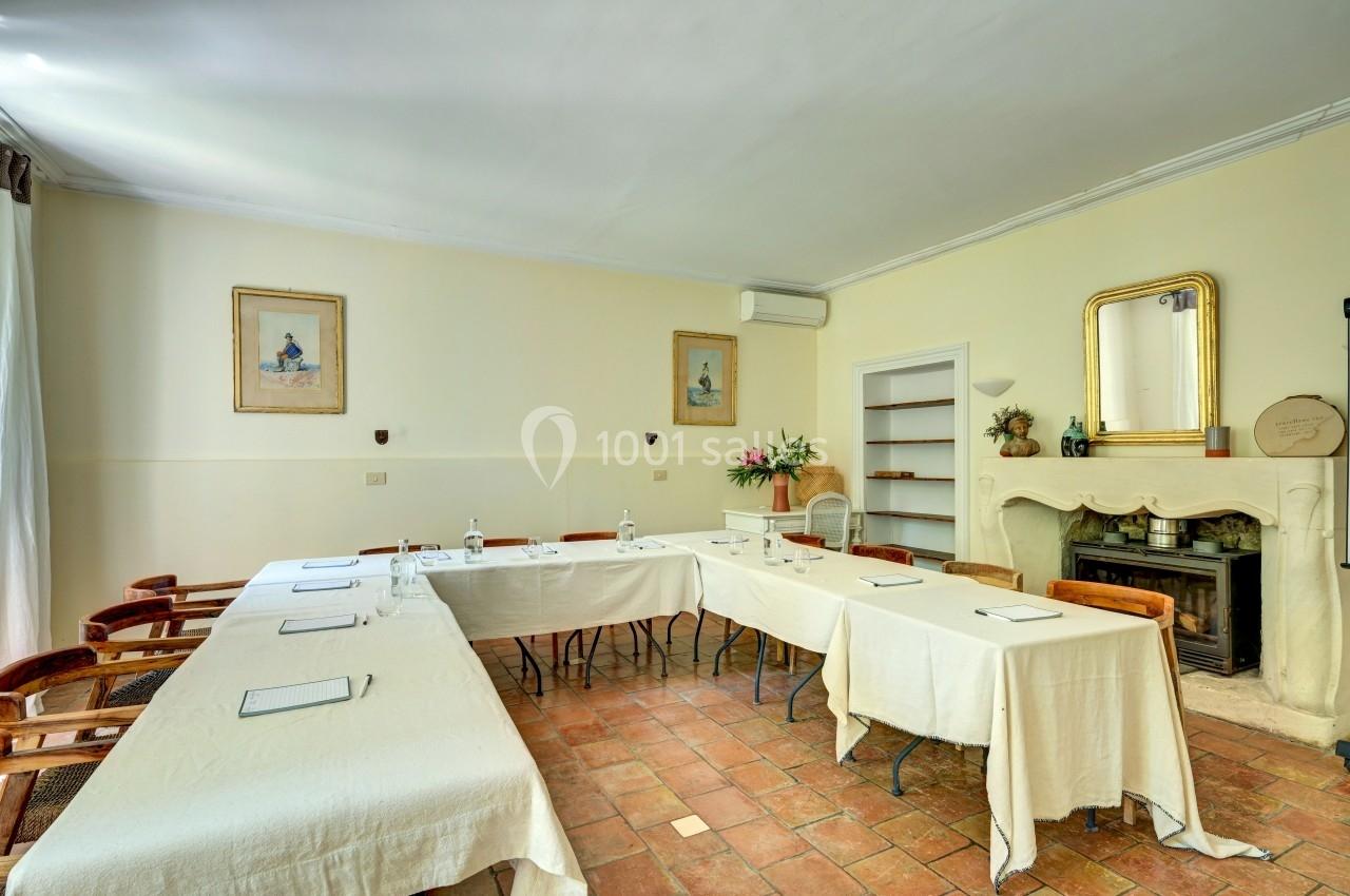 Salle de réunion lumineuse avec tables disposées en U, chaises en bois, cheminée et décorations murales.