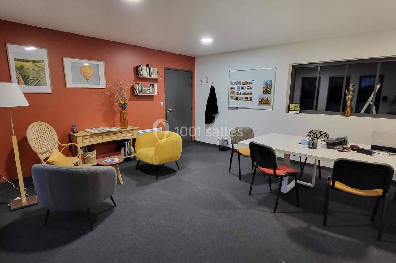 Salle de réunion lumineuse avec fauteuils, table blanche, étagères, mur rouge et tableau d'affichage.