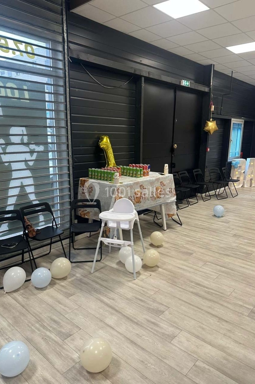 Salle décorée pour une fête avec ballons, table ornée de nappes à motif ’baby’ et chaises alignées.