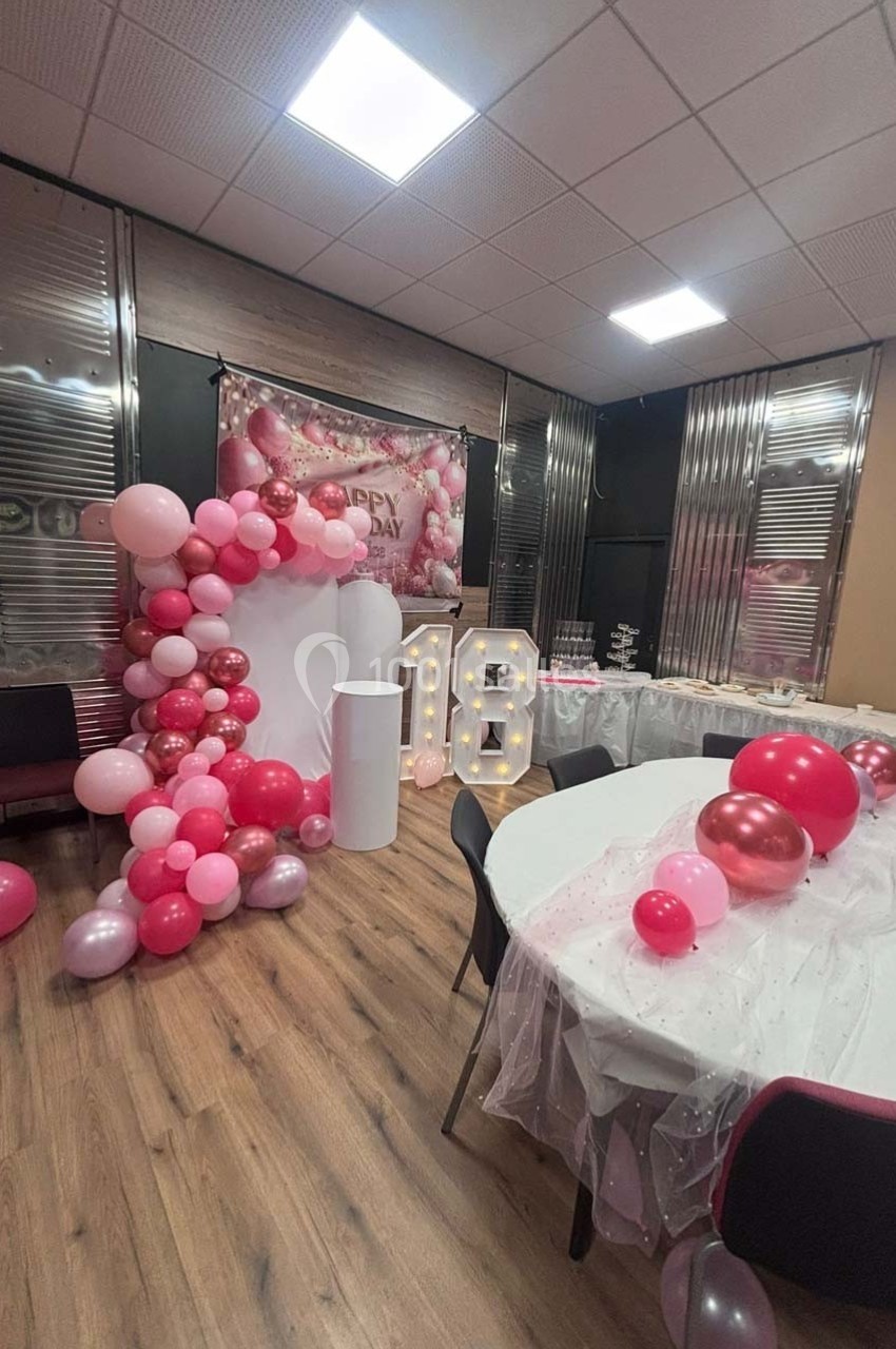 Salle décorée pour un 18e anniversaire avec ballons roses, guirlandes et chiffres lumineux ’18’.
