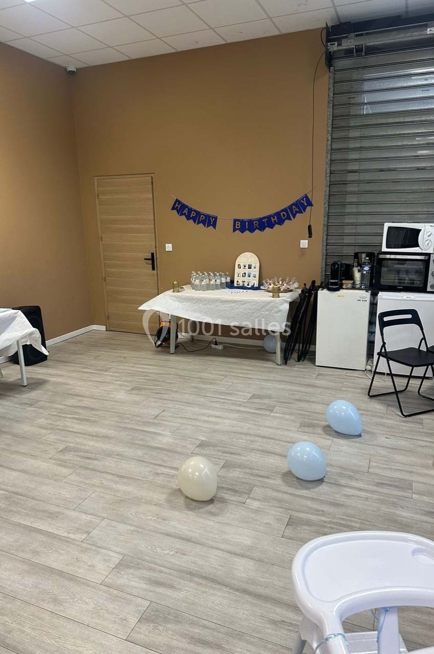 Salle décorée pour un anniversaire avec ballons au sol, une table dressée et une banderole ’Happy Birthday’.