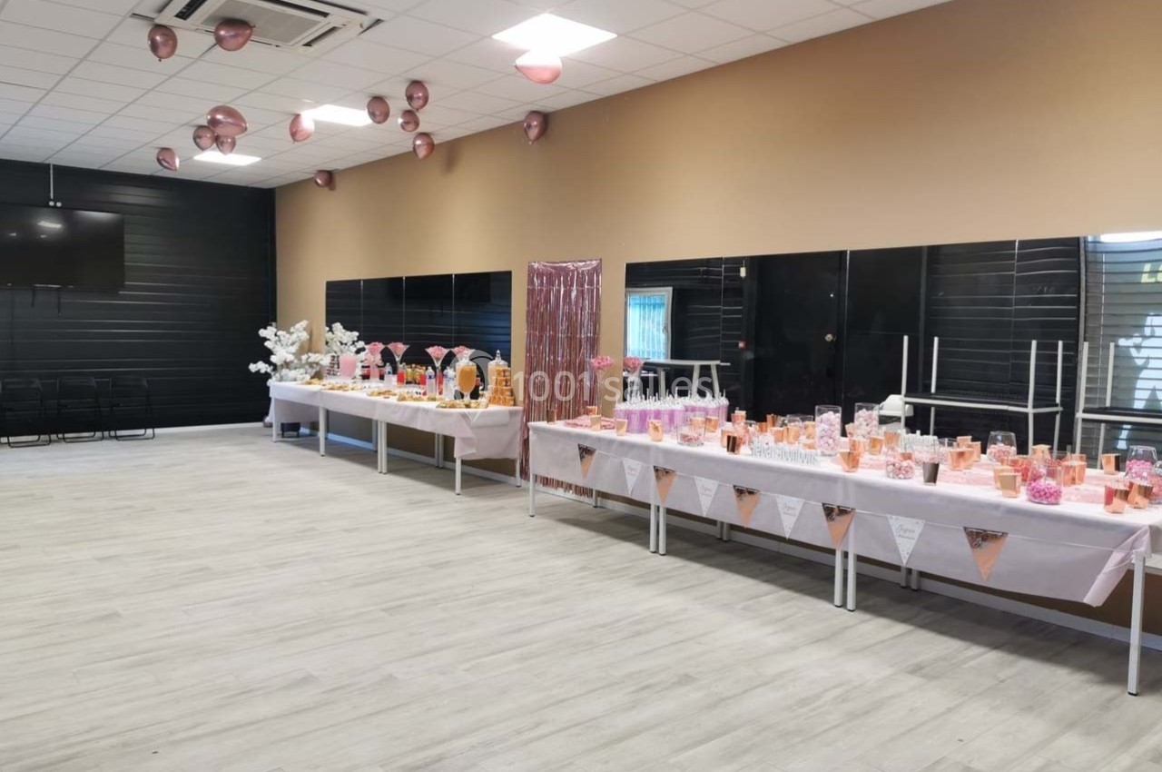 Salle décorée avec des ballons roses et des tables garnies de friandises et de boissons pour un événement festif.