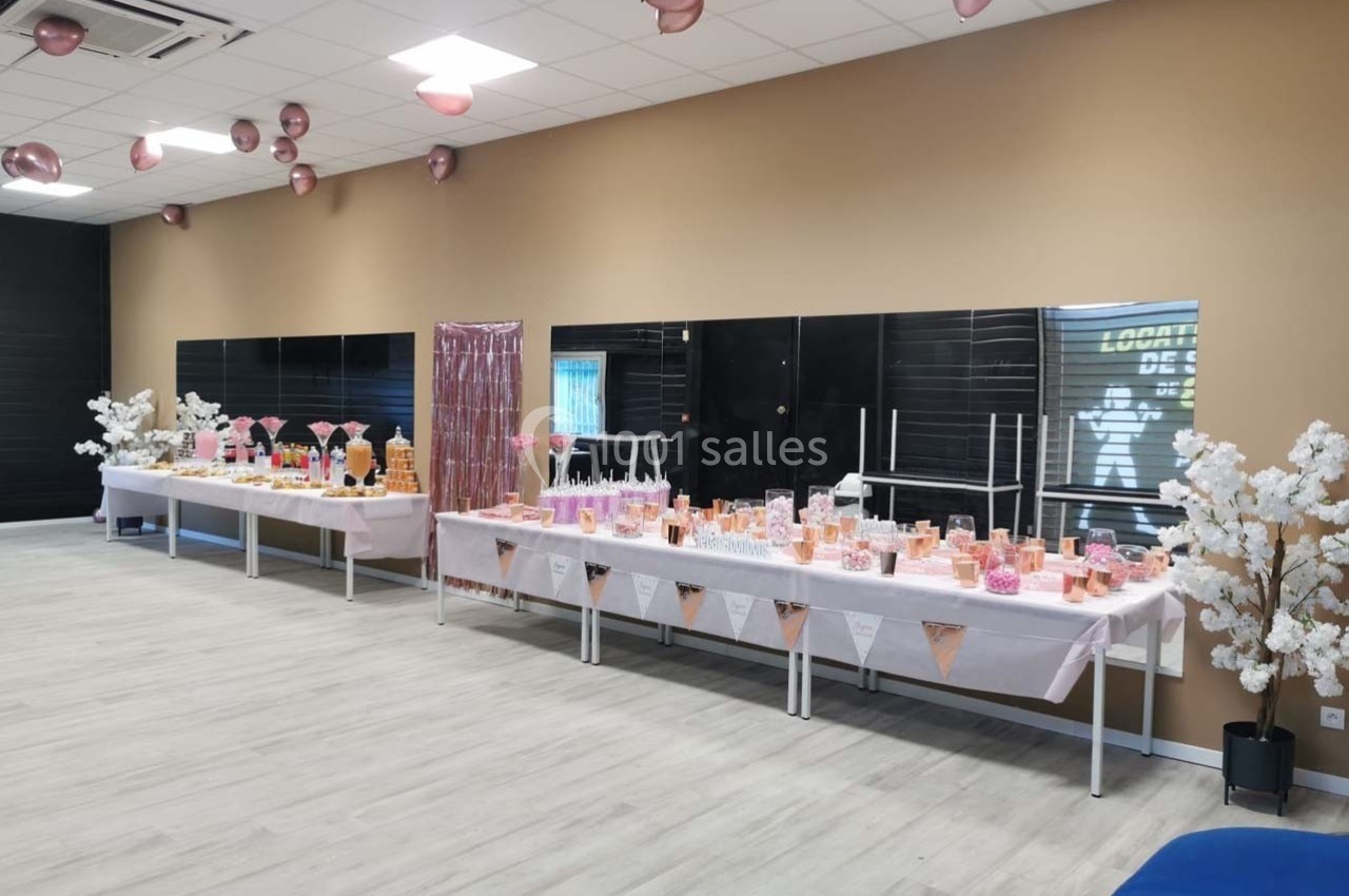 Salle décorée avec des ballons roses et des tables garnies de douceurs et boissons pour un événement festif.