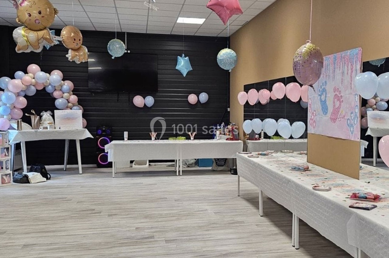 Salle décorée pour une fête avec ballons roses et bleus, tables dressées et décorations sur le thème des bébés.
