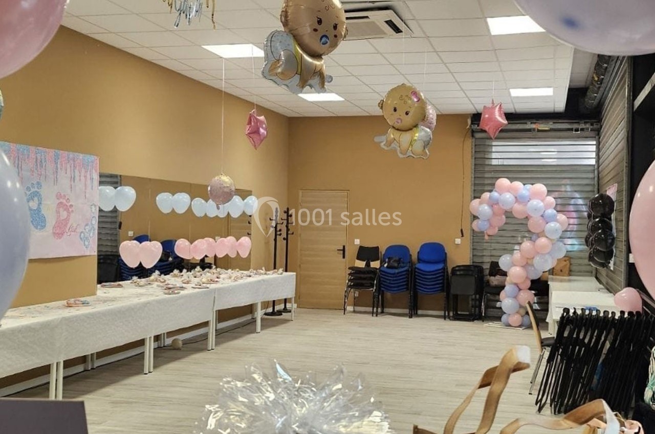 Salle décorée pour une fête prénatale avec ballons, table dressée et chaises empilées au fond.