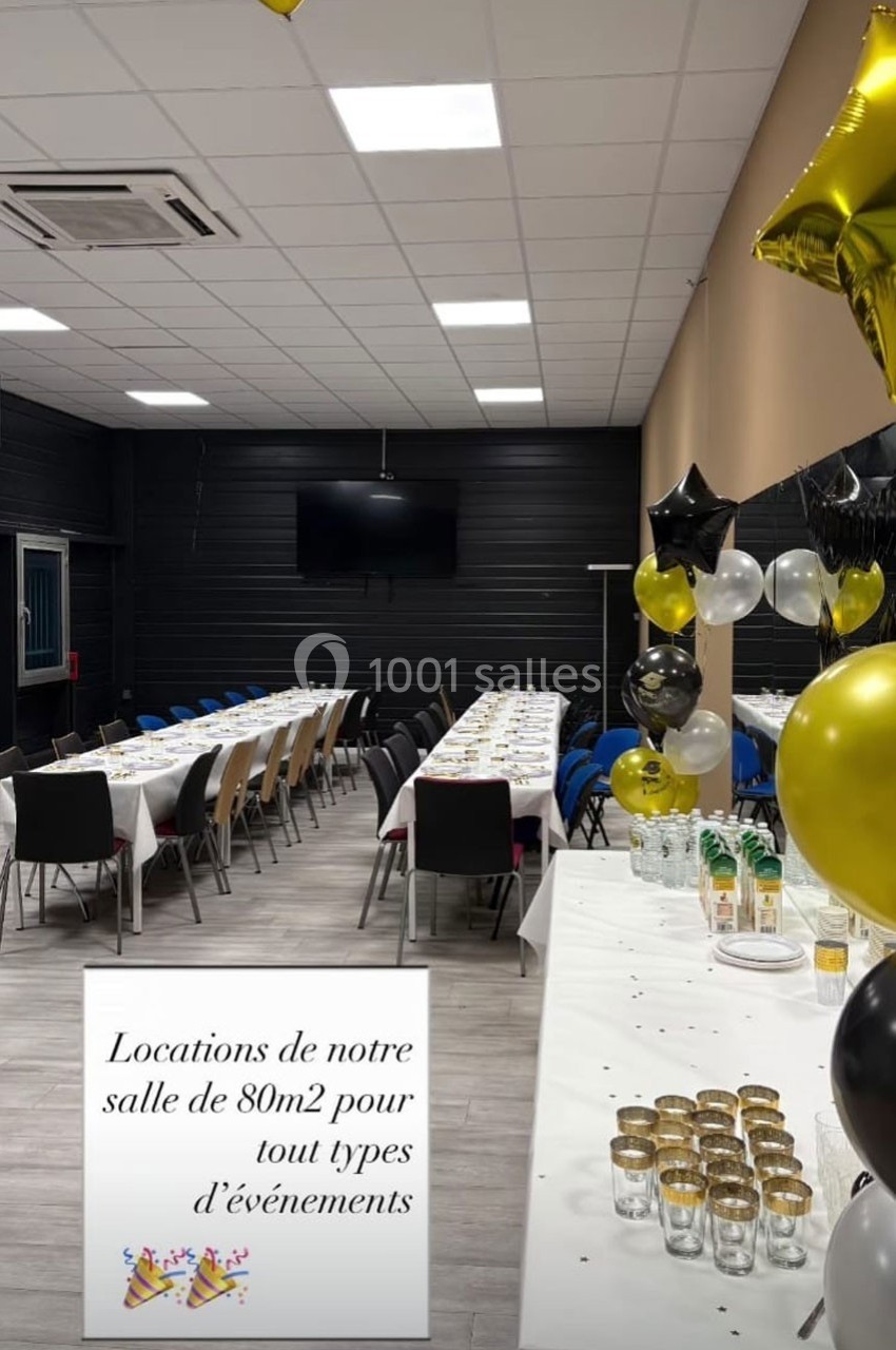 Salle décorée avec des ballons noirs et dorés, tables dressées pour un événement, avec chaises alignées.