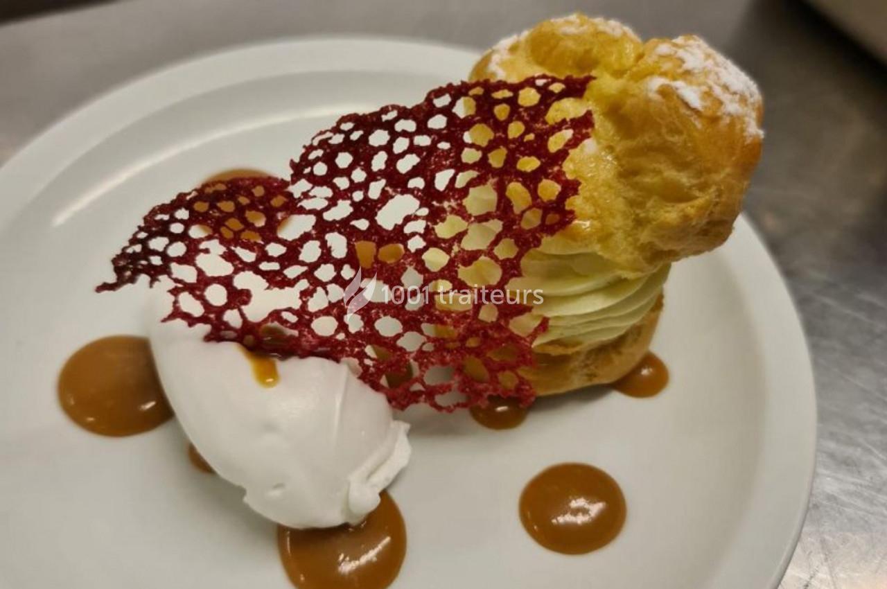 Pâtisserie composée d'une chouquette garnie, d'une quenelle de glace, d'une tuile rouge et de points de caramel.