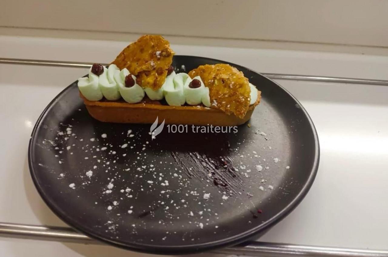 Tartelette garnie de crème verte, décorée de biscuits croquants et de petites baies, présentée sur une assiette noire.