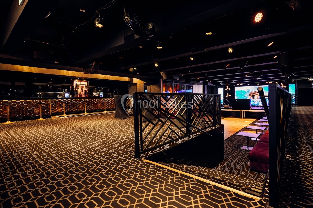 Intérieur d'un espace moderne avec moquette géométrique, séparations décoratives et éclairage tamisé.
