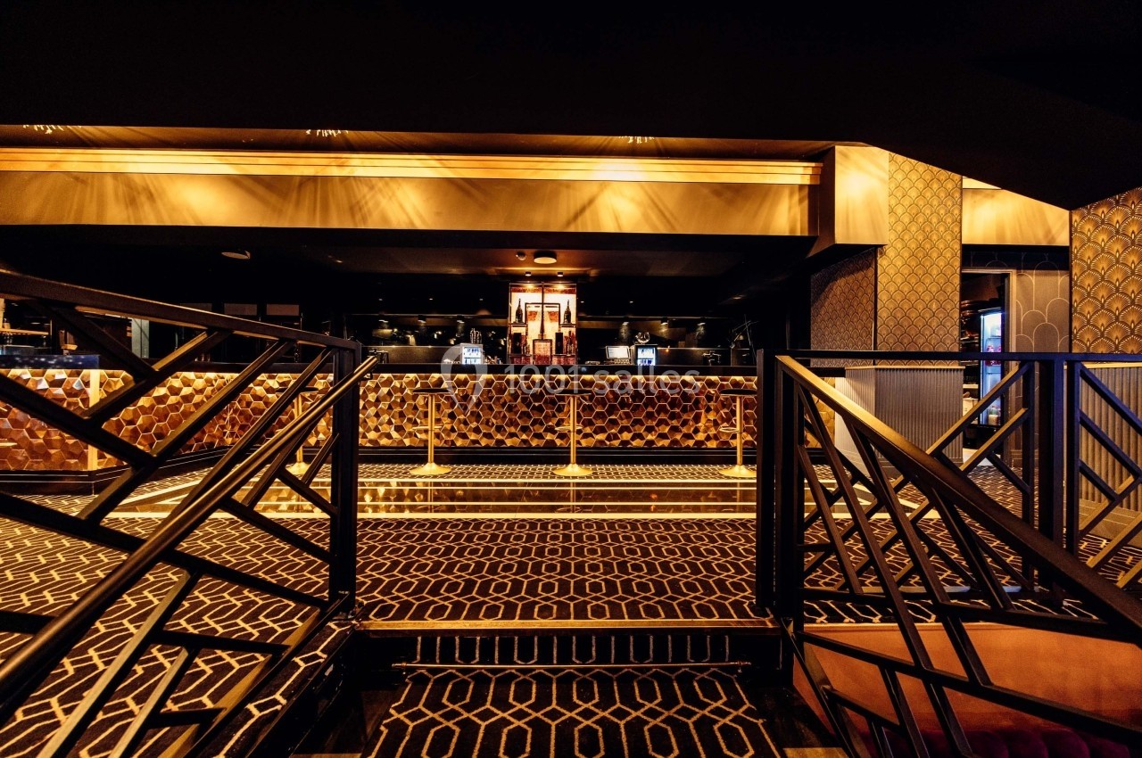 Intérieur d'un bar élégant avec des motifs géométriques au sol, des banquettes capitonnées et un éclairage chaleureux.