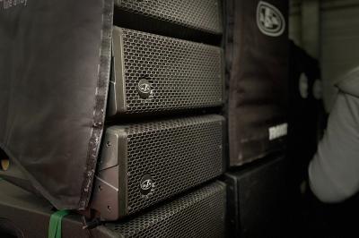 Miniature Ouest Spectacles et Techiques #7 Enceintes de sonorisation empilées dans une configuration de type line array, partiellement couvertes par des housses.