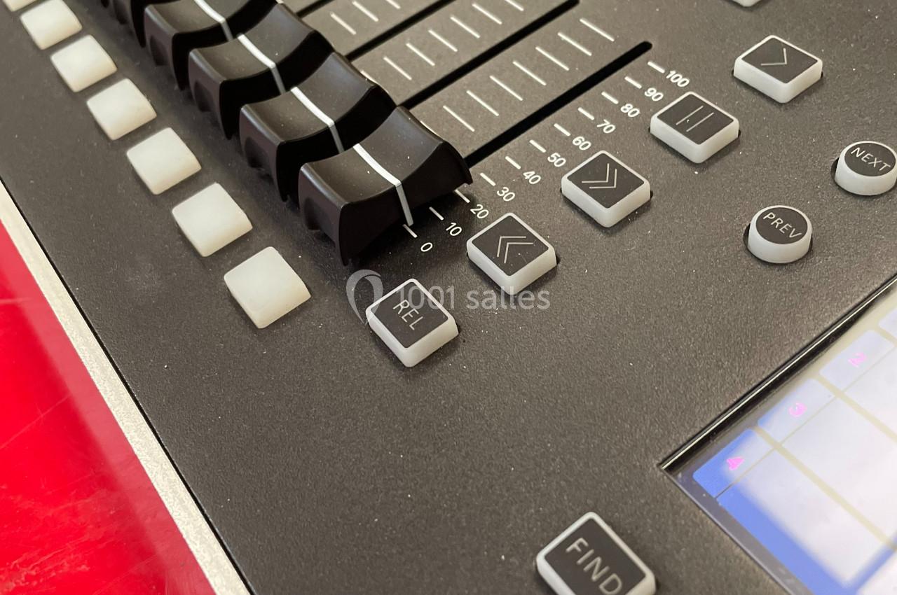 Table de mixage audio avec curseurs, boutons et écran tactile, posée sur une surface rouge.