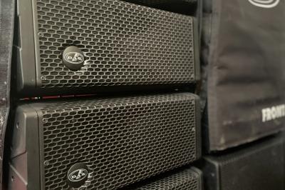 Enceintes de sonorisation empilées avec des grilles métalliques noires et une housse de protection partiellement visible.