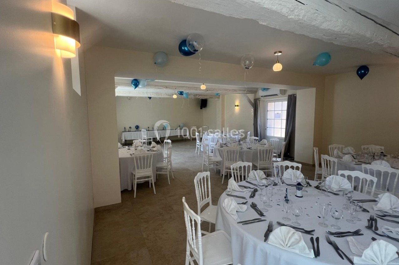 Salle de réception décorée avec des ballons bleus et blancs, tables rondes dressées avec nappes blanches et serviettes…
