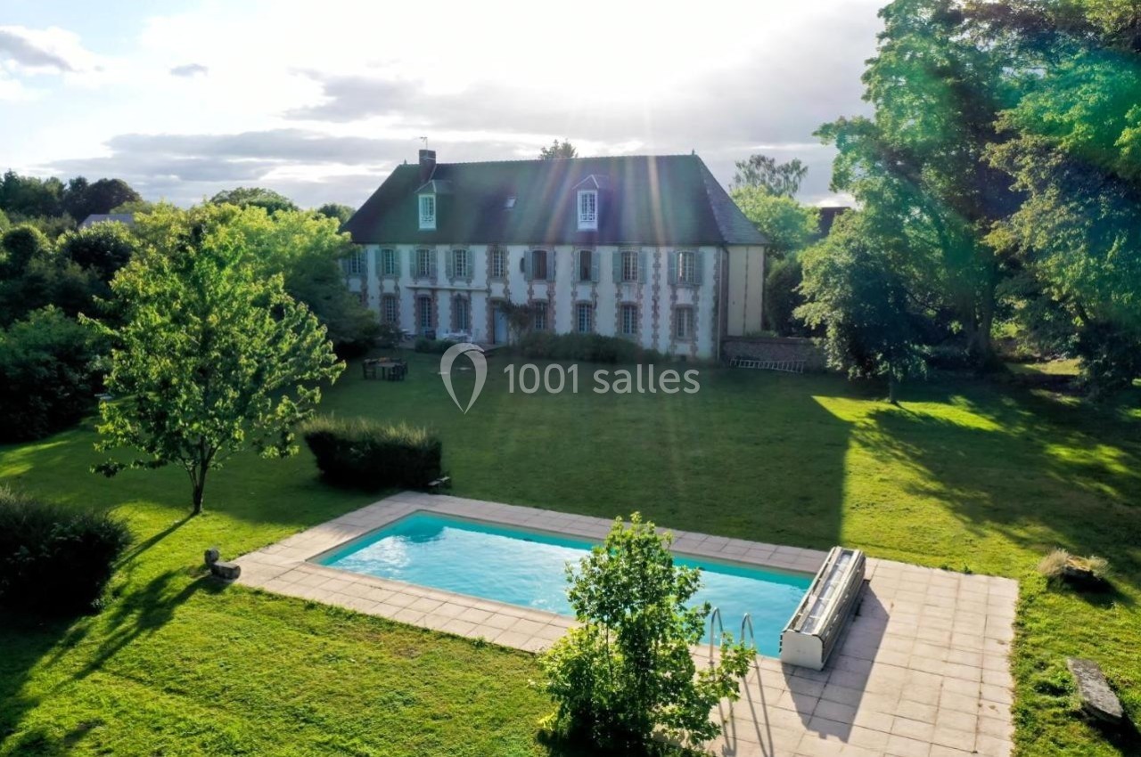 Grande maison en pierre entourée d'un vaste jardin verdoyant avec une piscine rectangulaire au premier plan.