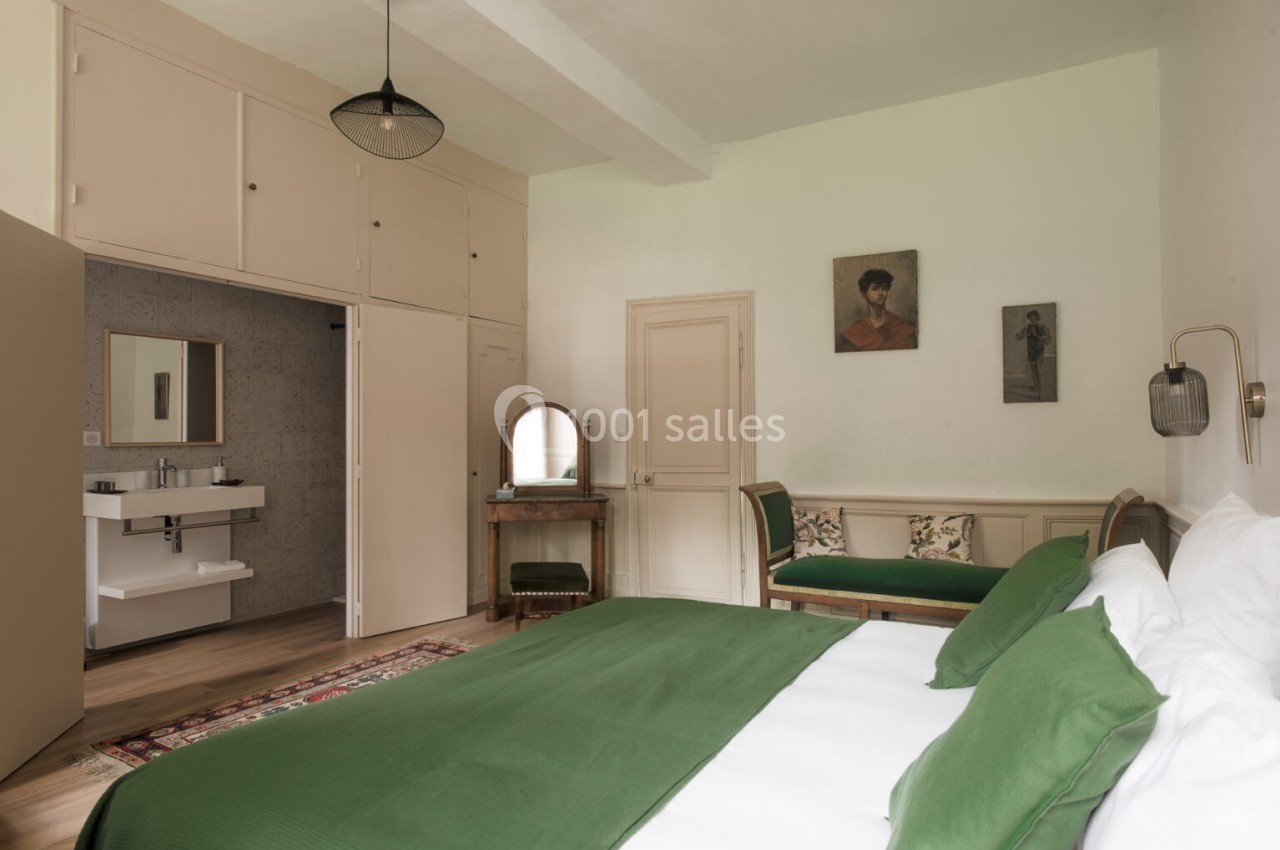 Chambre lumineuse avec lit double, linge de lit vert, mobilier en bois, salle d'eau attenante et décoration murale.