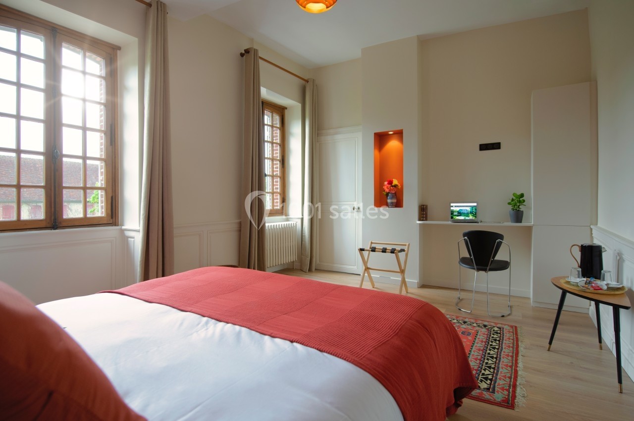 Chambre lumineuse avec lit double, bureau, chaise, fenêtre à carreaux et décoration sobre dans des tons chauds.