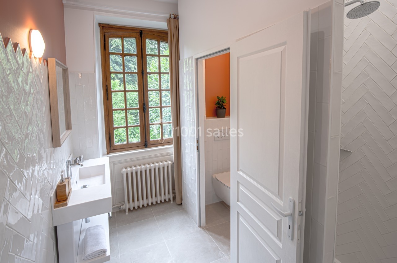 Salle de bain lumineuse avec lavabo, miroir, douche à l'italienne, toilettes séparées et fenêtre donnant sur un jardin.