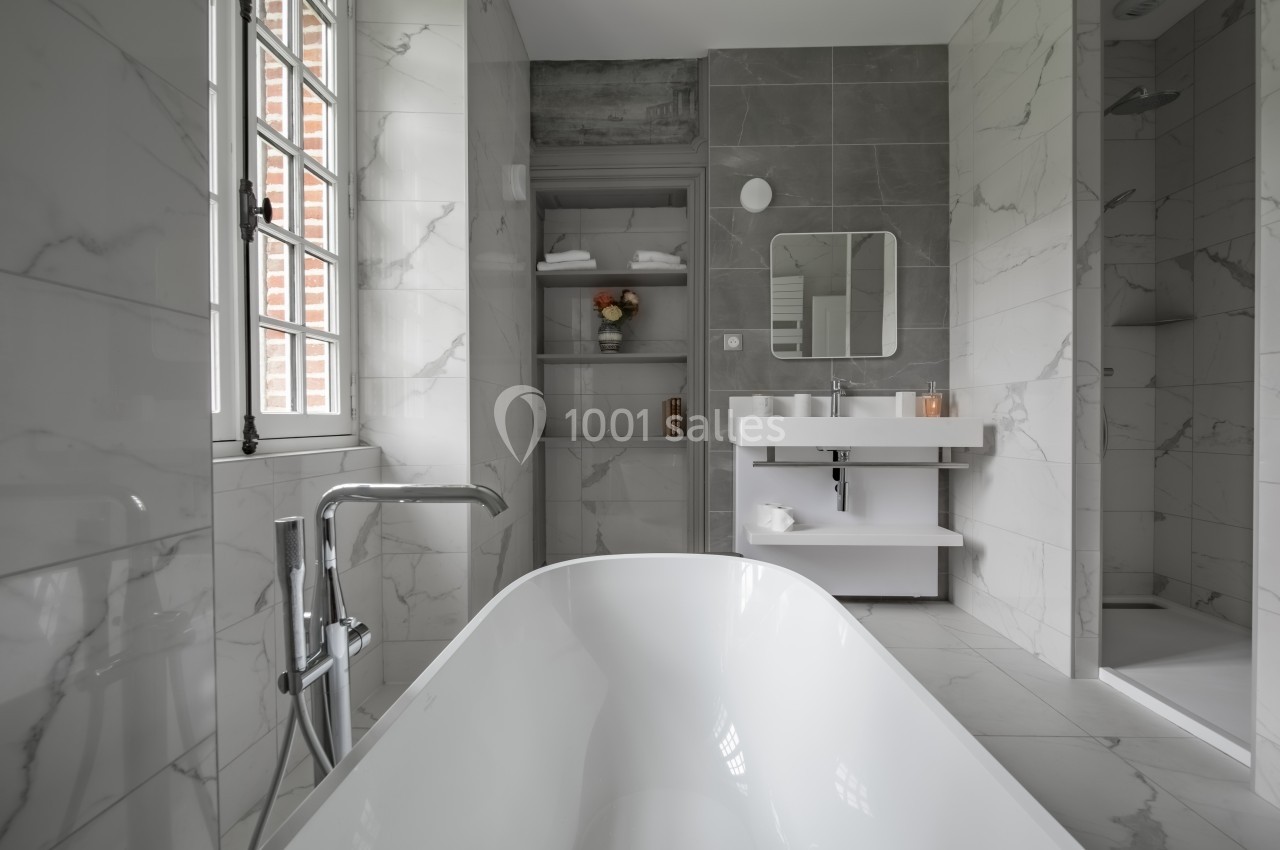 Salle de bain moderne avec baignoire, lavabo double, douche et étagères, murs en marbre et carrelage gris.