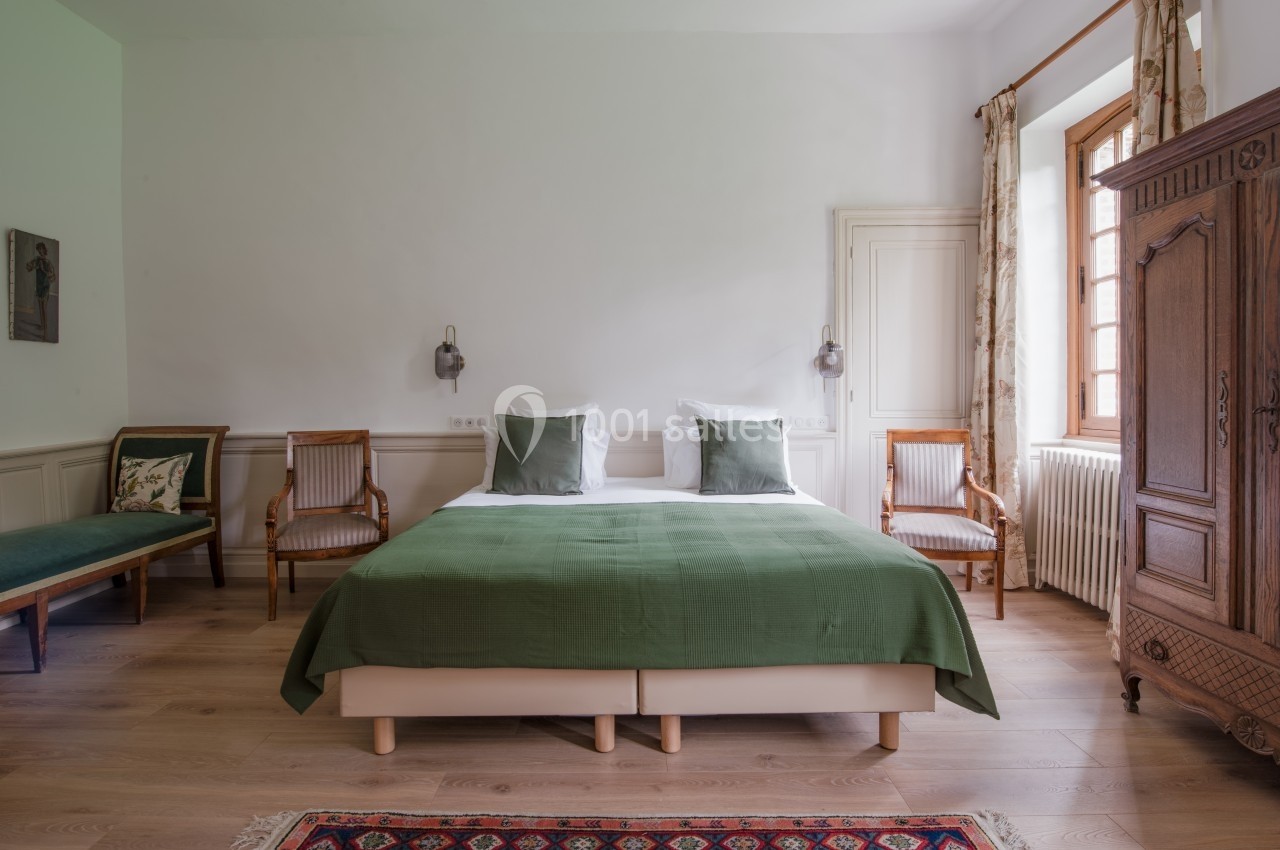 Chambre lumineuse avec lit double, couvre-lit vert, fauteuils en bois, armoire ancienne et tapis coloré.