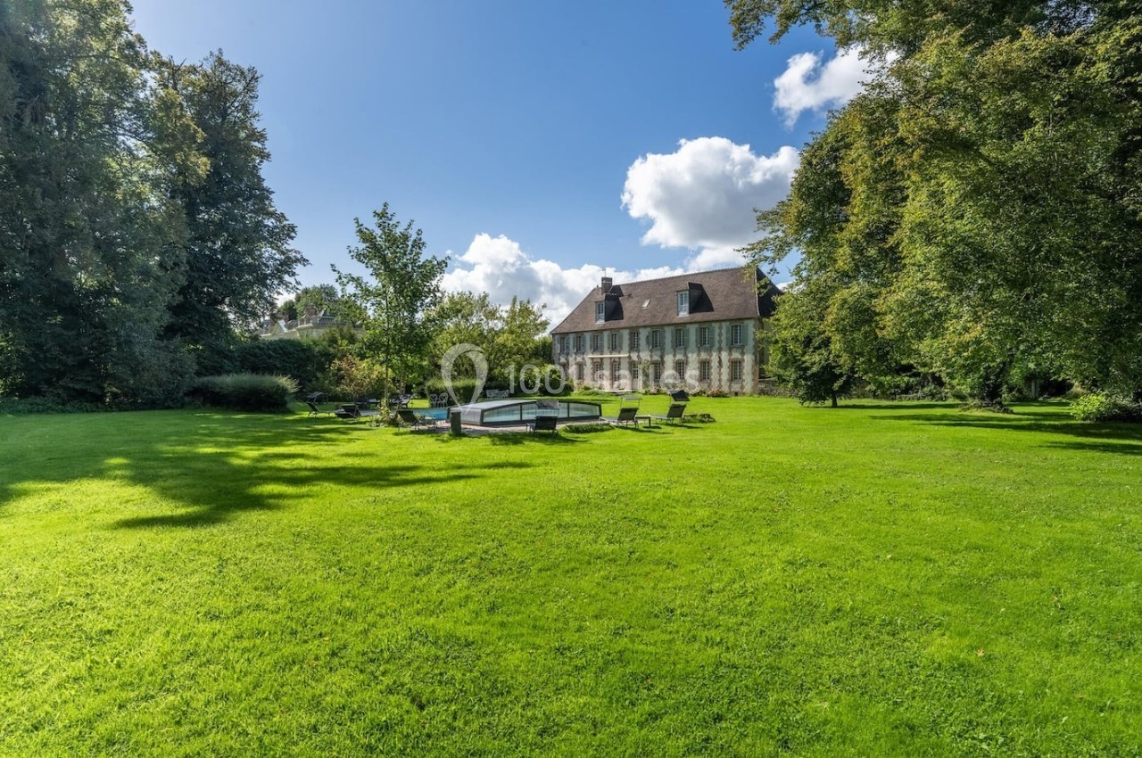 Grande maison en pierre entourée d'un vaste jardin verdoyant avec pelouse, arbres et mobilier extérieur.