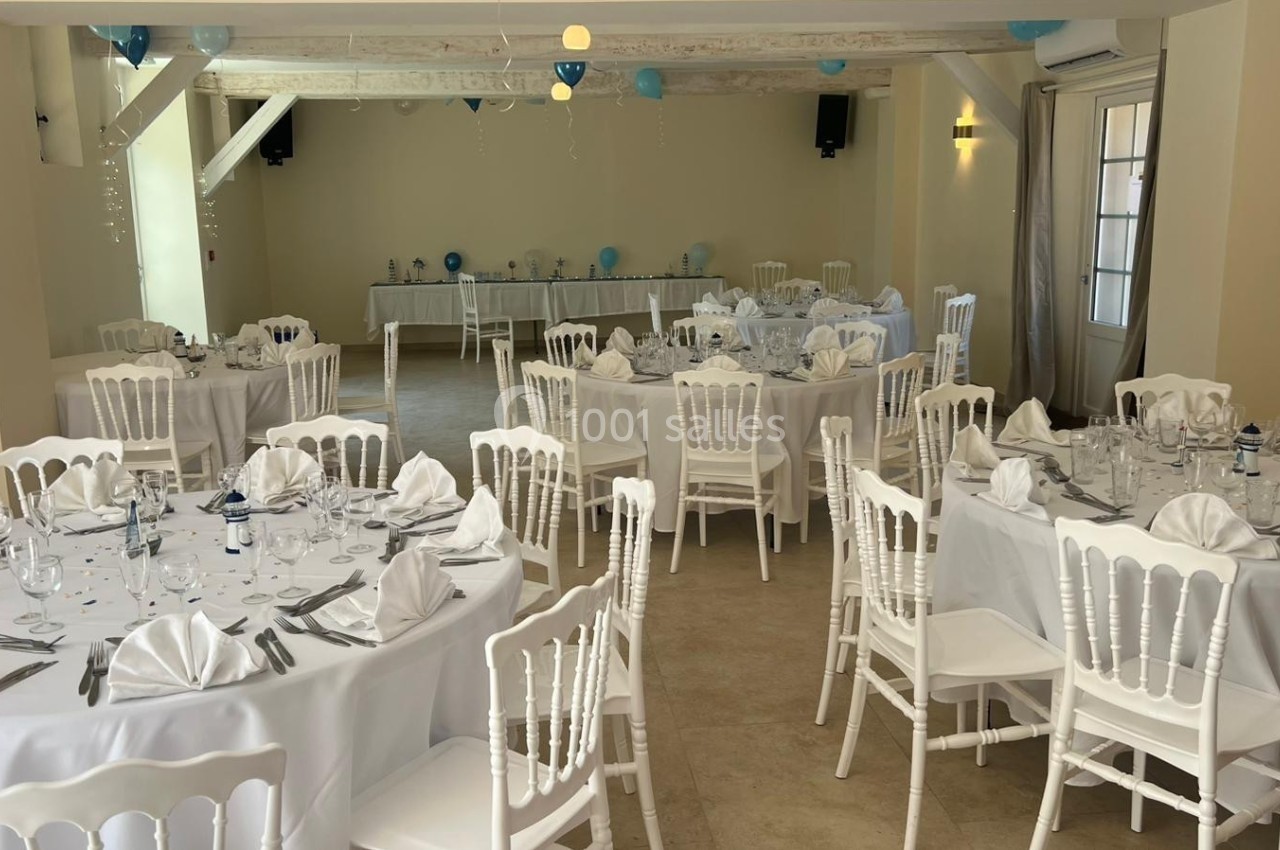 Salle de réception décorée avec des tables rondes dressées de nappes blanches et ornées de serviettes pliées.