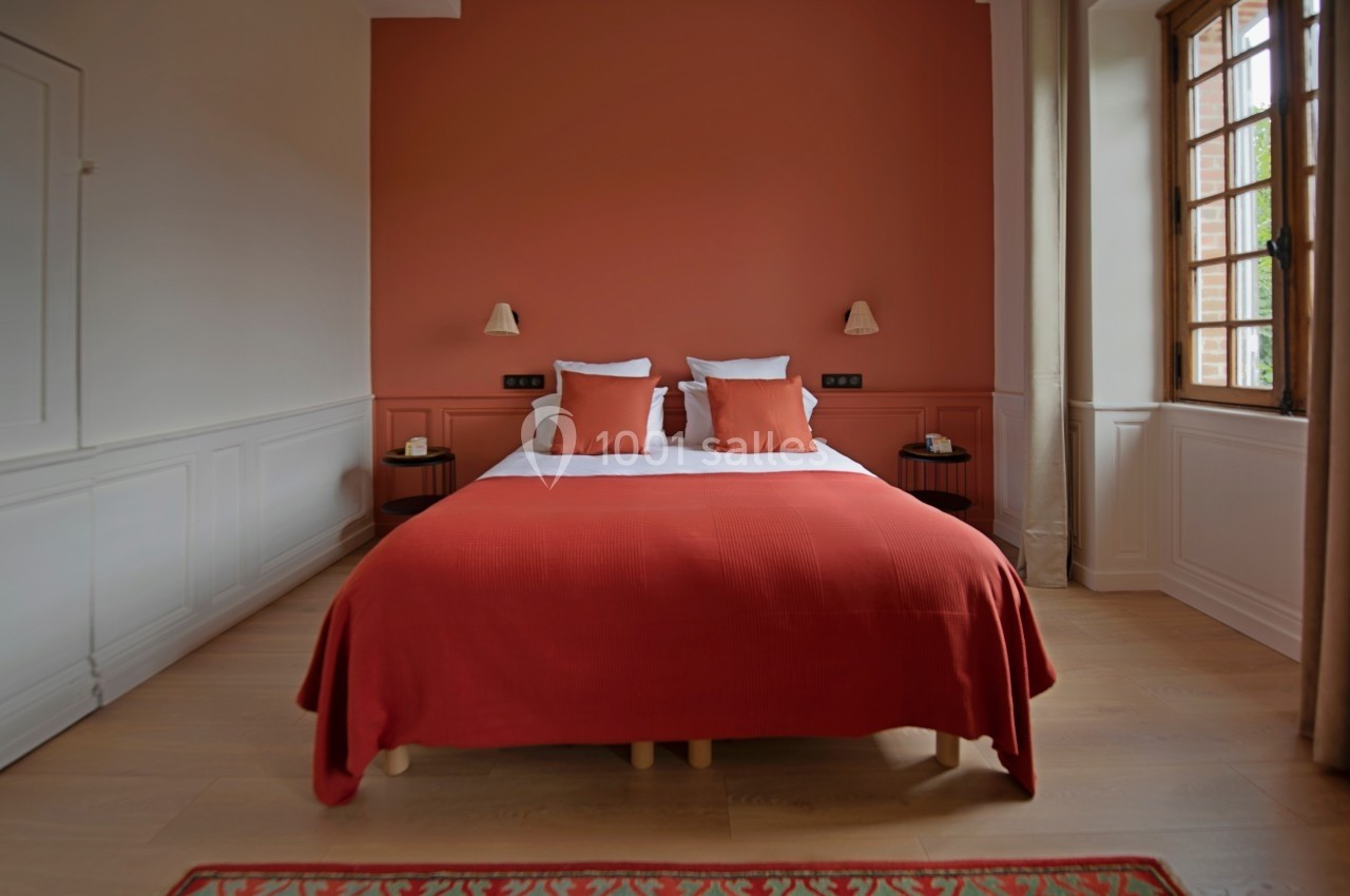 Lit double avec couverture rouge et coussins assortis, encadré par deux tables de chevet, dans une chambre lumineuse.