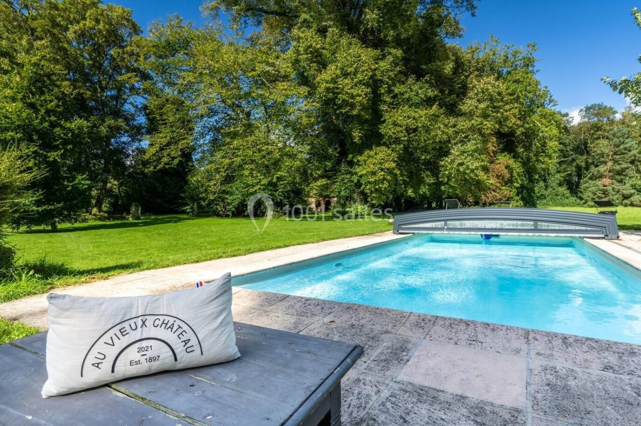 Piscine extérieure entourée de verdure avec un coussin posé sur une table en pierre au premier plan.
