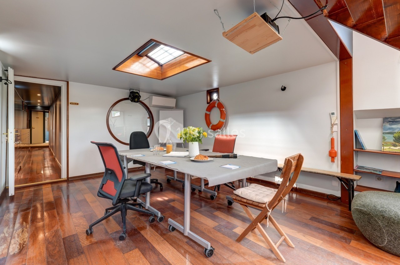 Salle de réunion lumineuse avec table, chaises, parquet en bois et décoration nautique.
