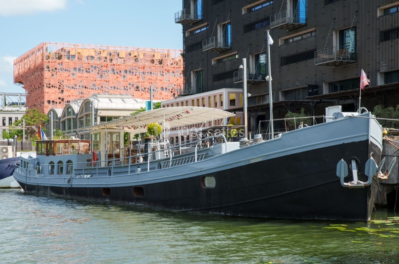 Bateau amarré sur un canal, entouré de bâtiments modernes et d'une architecture colorée en arrière-plan.
