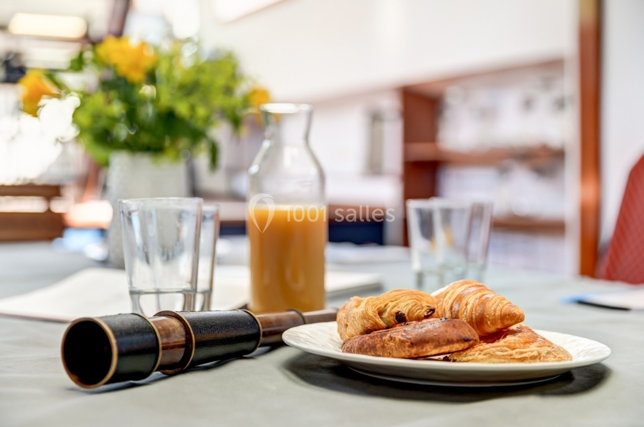 Assiette de viennoiseries avec croissant, pain au chocolat et jus d'orange sur une table, en arrière-plan un bouquet.