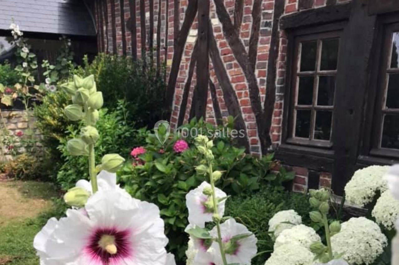 Fleurs blanches et roses devant une maison en briques et colombages avec des fenêtres en bois.