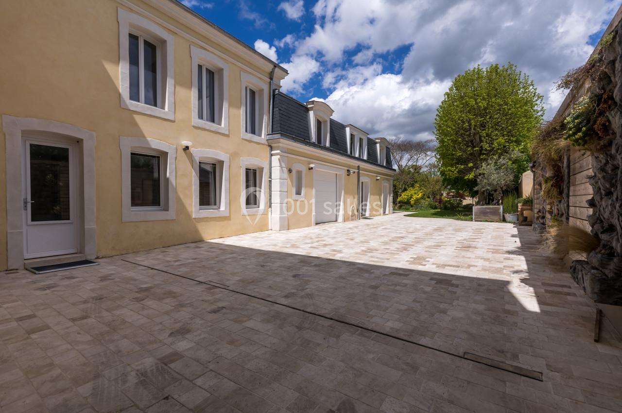 Cour pavée en pierre claire entourée d'un bâtiment jaune à deux étages et d'un mur végétalisé sous un ciel partiellement…
